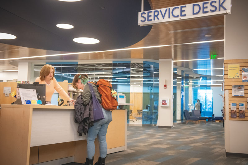 A young woman standing at a service desk, getting help from a librarian.