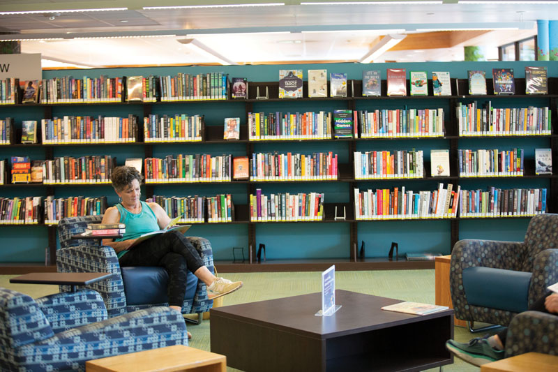 Woman sitting in a chair with a full bookshelf behind her.