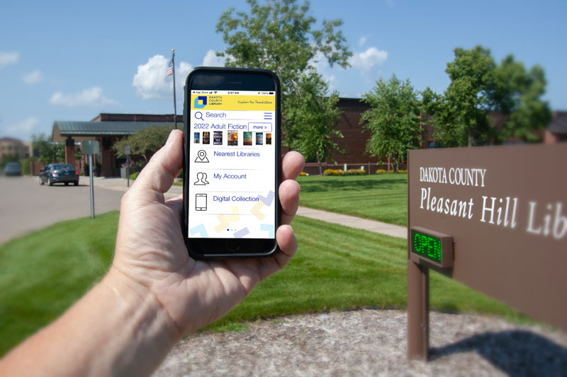 Person holding cellphone up displaying mobile app outside of library.