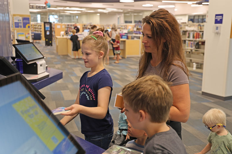 Adult and children using the selfcheck machine to check out items.