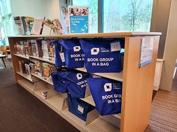 Bookshelf with blue bags of book group kits on them.