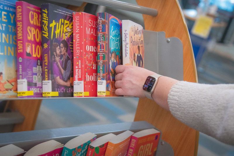 Person reaching for a book on a shelf.