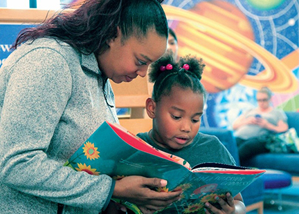 Adult and child reading book in library.