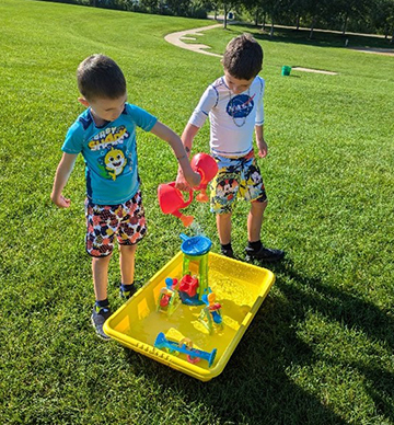 Two boys playing with water table on the grass at a library location.