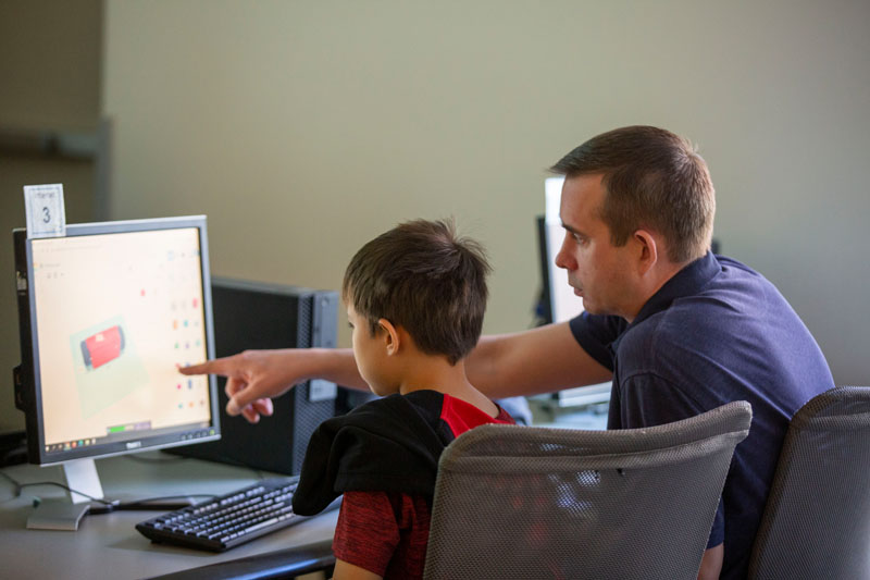 Adult male pointing to a computer screen with a child intently watching.