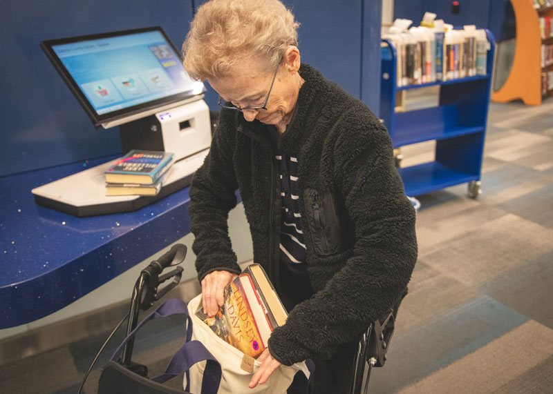 Older adult at self-check out machine loading books into a bag.