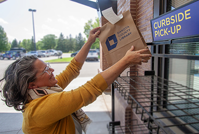 Woman grabbing a bag of books of a tall shelf outside.