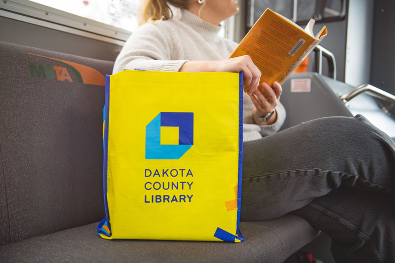 A woman on a bus with a Dakota County Library bag next to her.