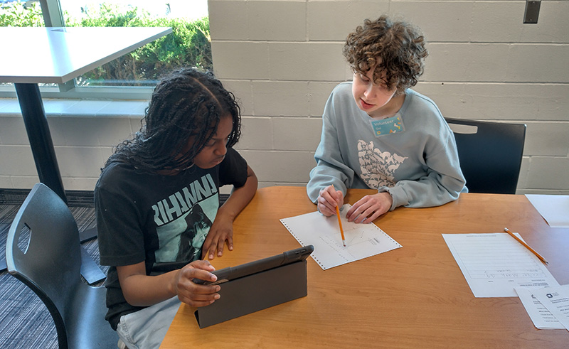 Two people doing homework together, one helping the other.