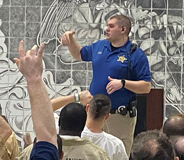 Officer speaking in front of a group of seated inmates.