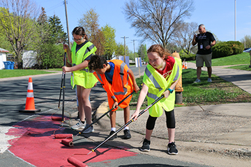 Students painting a crosswalk to create a safer crossing.