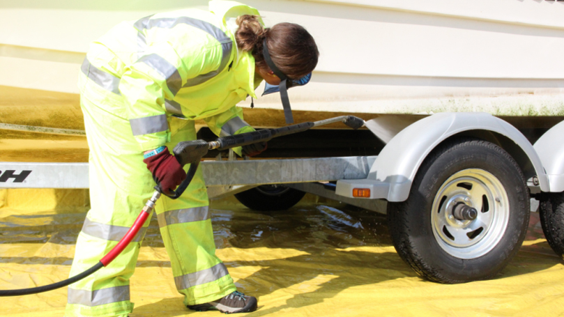 Woman in bright yellow suit cleaning a boat with a power washer.