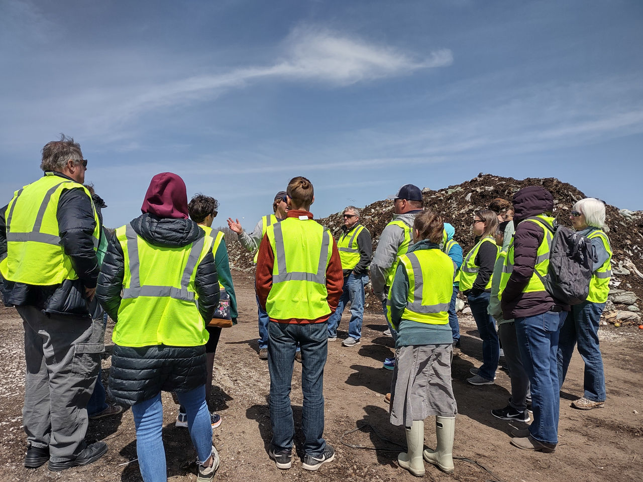 A group of people smiling and standing in front of a large pile of compost.