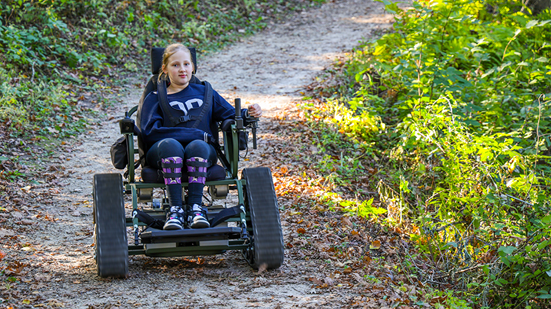 A girl using an all-terrain track chair on a Lebanon Hills hiking trail.