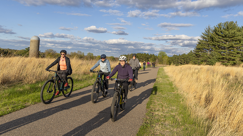 Group of people riding bicycles along a paved trail.