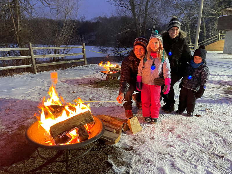 A family stands near a recreational bonfire during the wintertime.