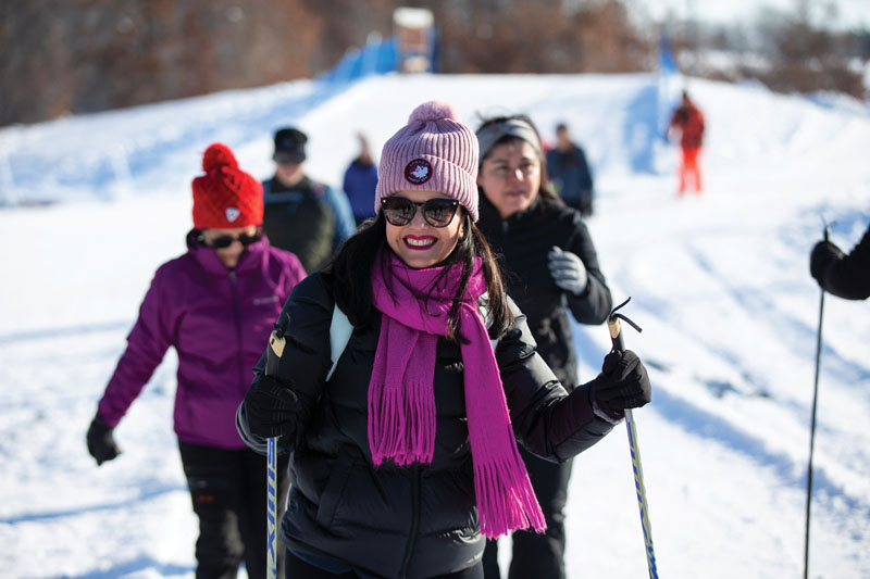 A smiling woman going cross-country skiing with other people behind her.