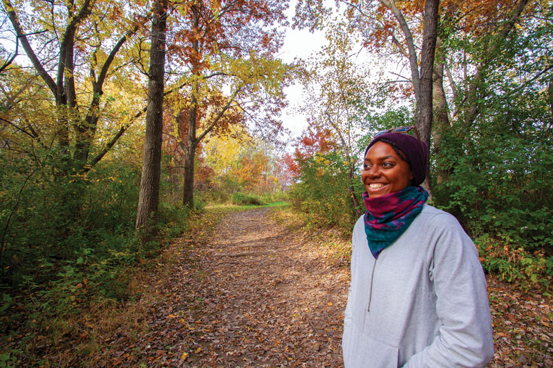 A smiling woman on a leaf-covered hiking trail in the fall.