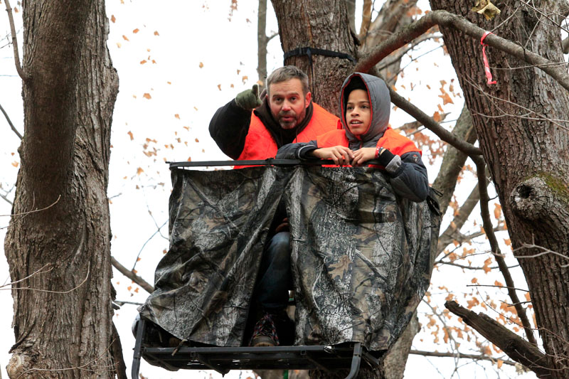 A man and a boy wearing blaze orange in a tree stand.