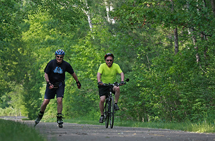 A man in-line skating next to another man riding a bicycle.