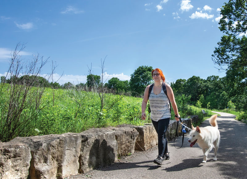 A woman walking her dog on a paved trail.