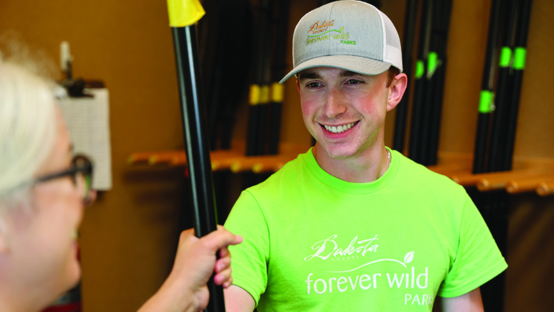 A man hands a paddle to a woman inside an equipment building.