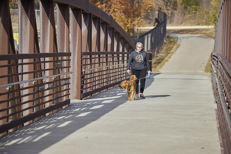 Woman walking her dog across bridge on Byllesby Dam Trailhead.