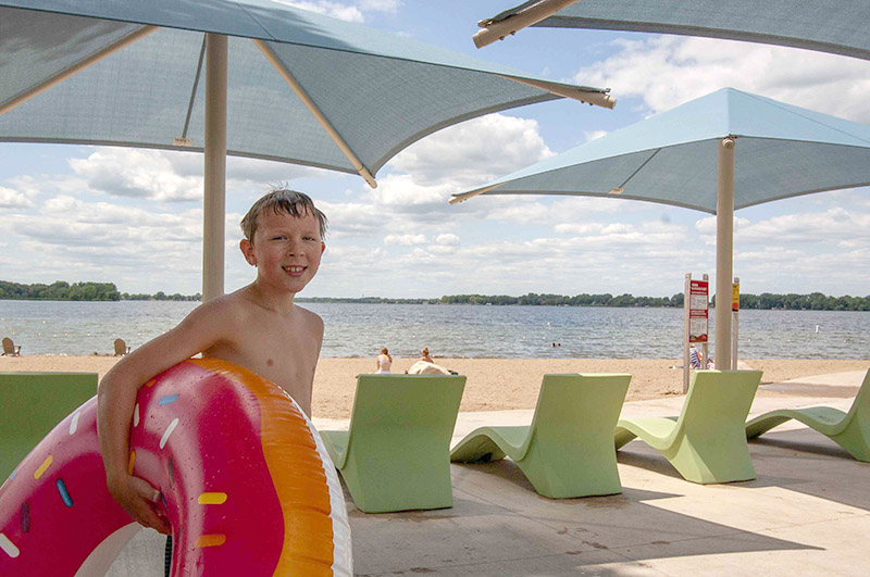 Boy holding an inner tube under an umbrella at Lake Byllesby Beach.
