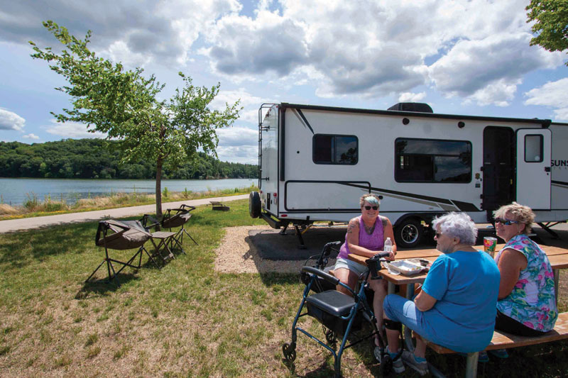 Three women sitting at a picnic table in front of an RV.