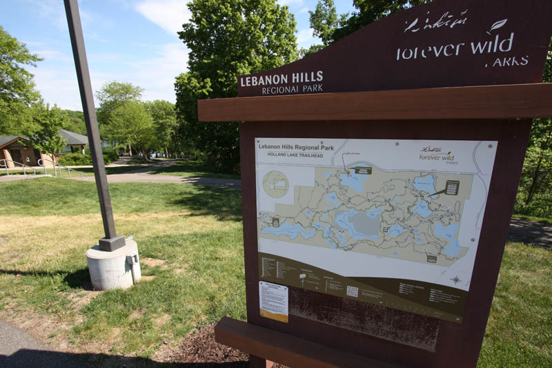A park kiosk sign with a map on it near a light pole.
