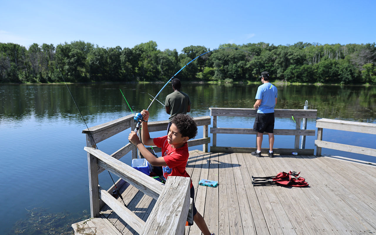 A boy casting a lure into a lake from a fishing pier.