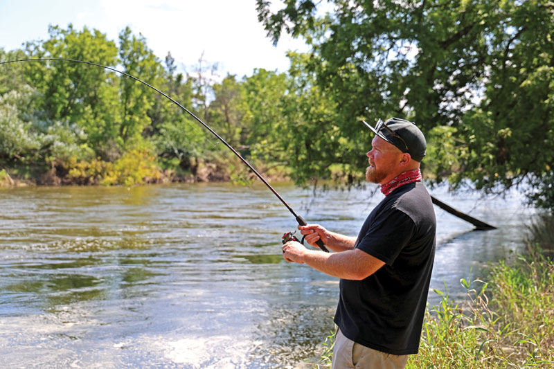 A man standing at the edge of a river fishing