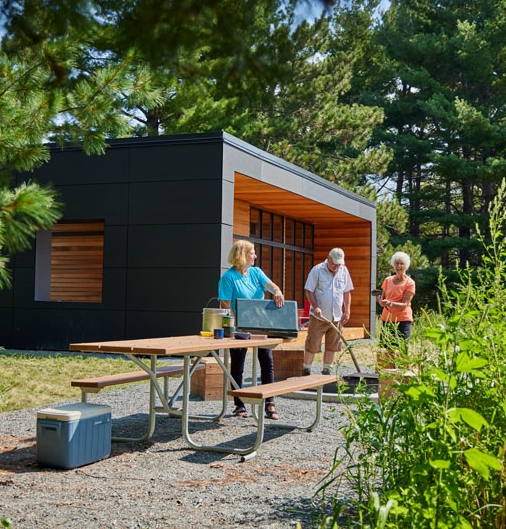 Three people setting up a picnic table in front of a camper cabin.