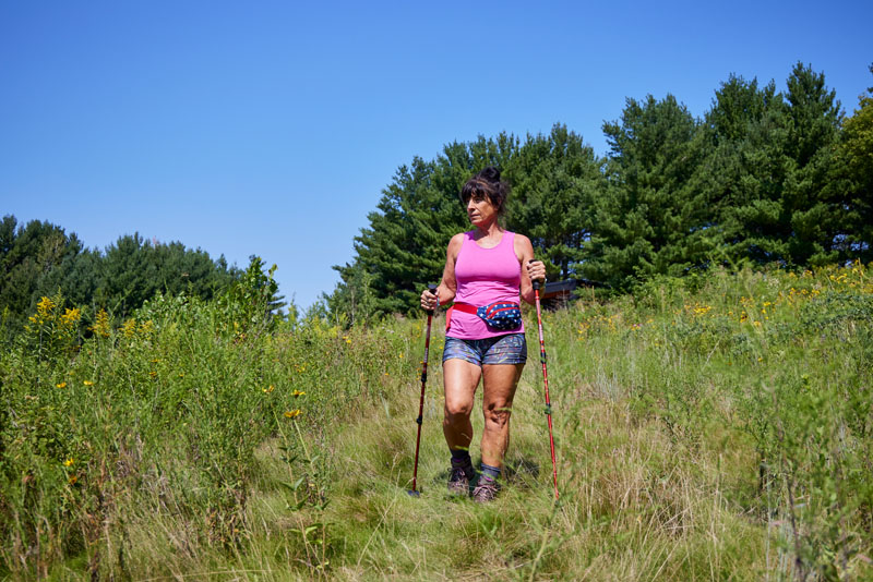 Woman hiking on grass path with walking sticks