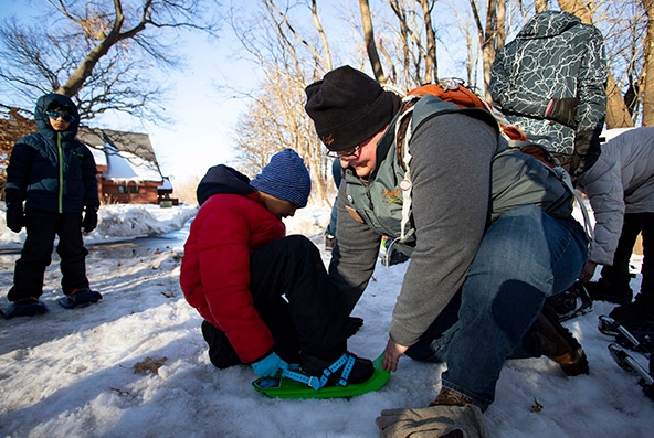 A park naturalist helping a student put a snowshoe on.