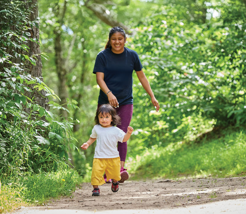 Young child walking down a trail with a woman following.